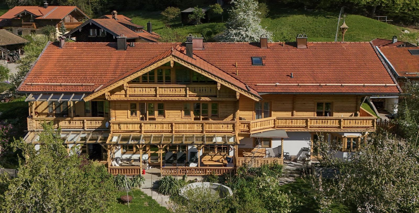 Frontalansicht des Gästehaus Berghof mit umlaufenden Holzbalkonen und blühendem Frühlingsgarten